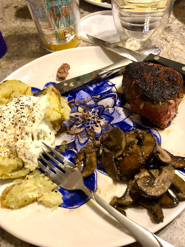 A white and blue plate topped with filet mignon, baked potato and mushrooms from RVing With Family
