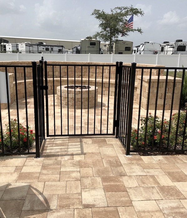 A black fence and gate with a stone fire pit at Sunkissed Village RV Resort