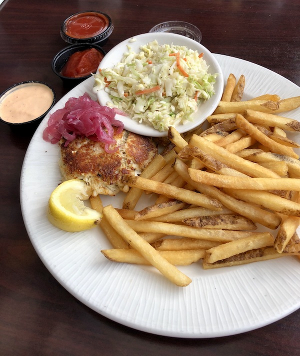 A white plate topped with a crab cake, fries, coleslaw and lemon wedge in Chesapeake Virginia