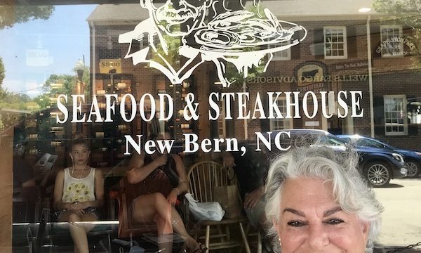 A silver haired woman in a tropical print dress in front of restaurant window in New Bern NC