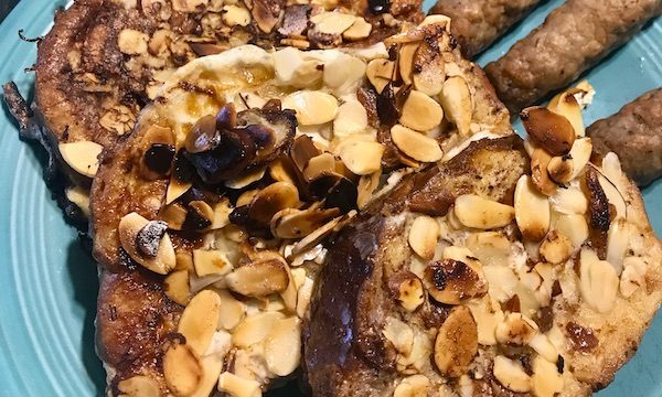 A turquoise plate topped with almond covered French toast and sausage links cooked at North River Campground NC