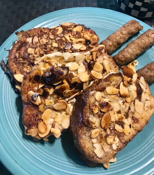 A turquoise plate topped with almond covered French toast and sausage links cooked at North River Campground NC