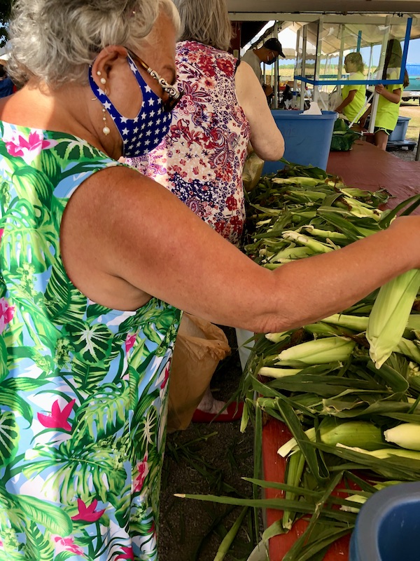 A woman in a tropical print dress selecting fresh corn near North River Campground NC