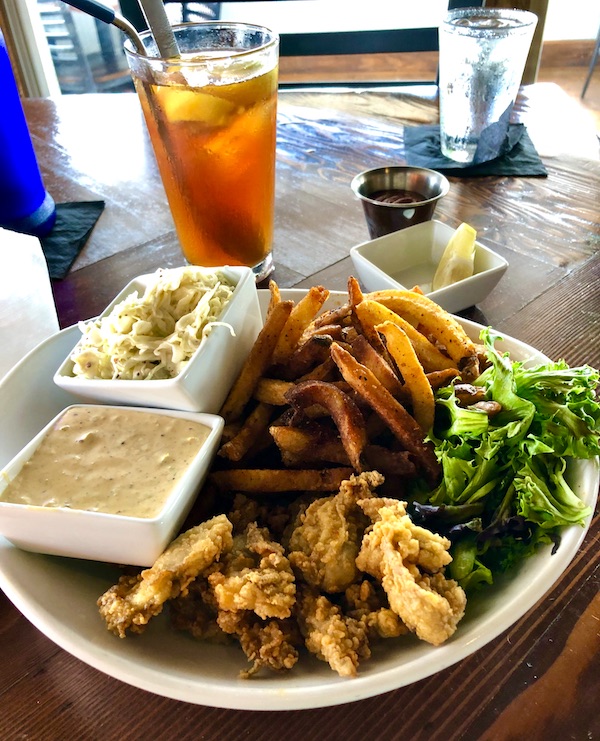 A white plate topped with fried oysters, fries, coleslaw and greens at a restaurant in OBX Outer Banks North Carolina