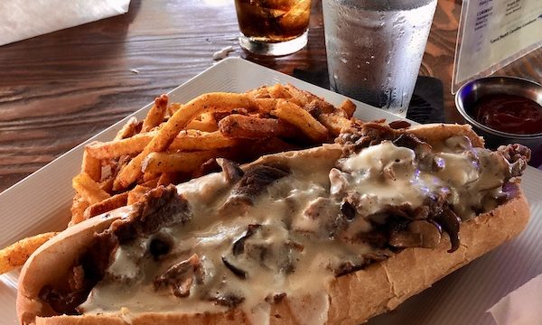 A square white plate topped with a cheesesteak and fries at a restaurant in OBX Outer Banks North Carolina