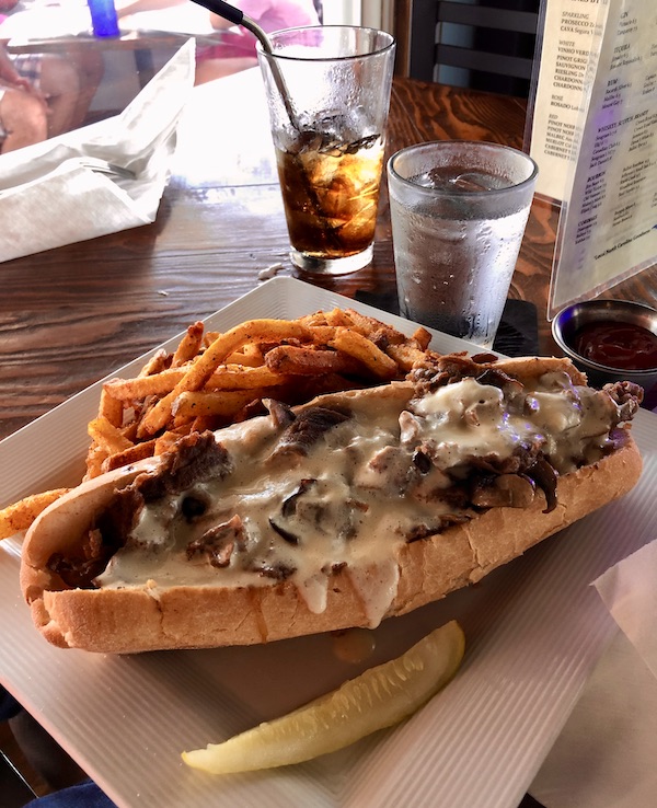 A square white plate topped with a cheesesteak and fries at a restaurant in OBX Outer Banks North Carolina