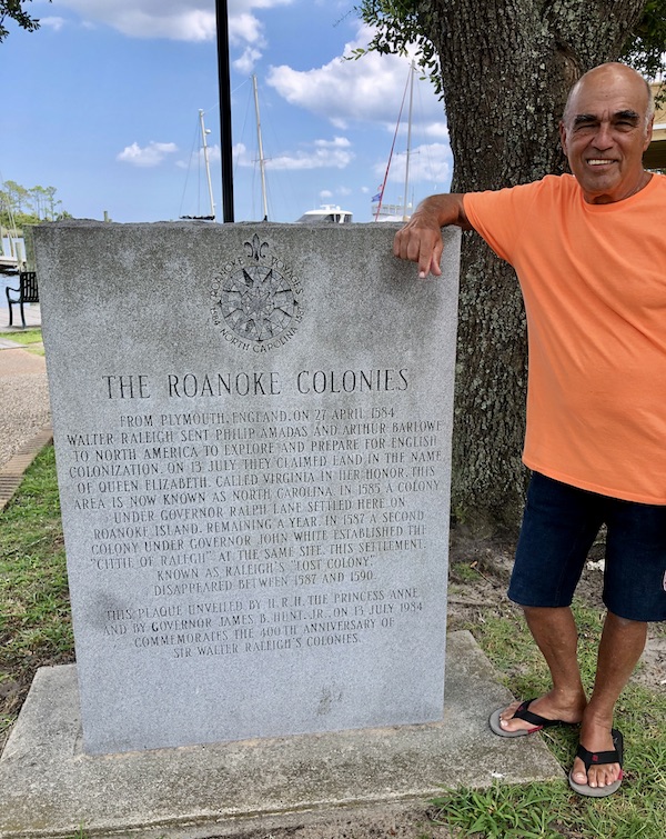A stone monument with the story of the Roanoke Colonies and a man in an orange shirt standing next to it in OBX Outer Banks North Carolina
