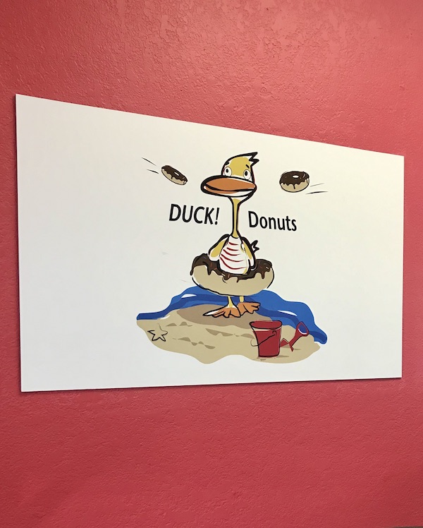A red wall with a white poster of a duck with a donut as a float at OBX Outer Banks North Carolina