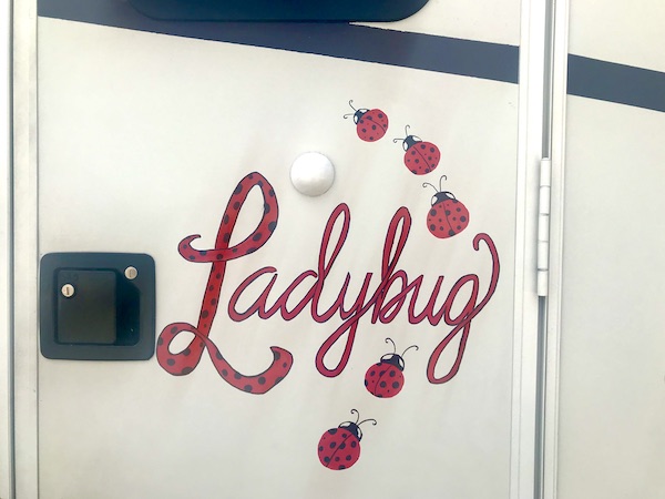 An RV entry door with the name Ladybug and some ladybugs painted in red and black from RV Renovations Complete The Big Reveal