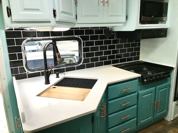 An RV kitchen with black backsplash, white counter and aqua cabinets from RV Renovations Complete The Big Reveal