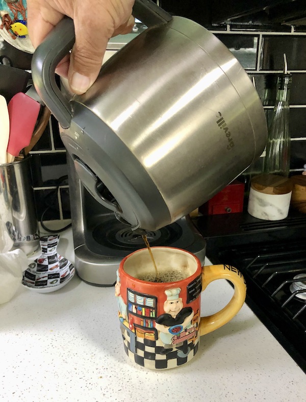 A metal coffee pot pouring coffee into a colorful mug from RetroFuture Coffee