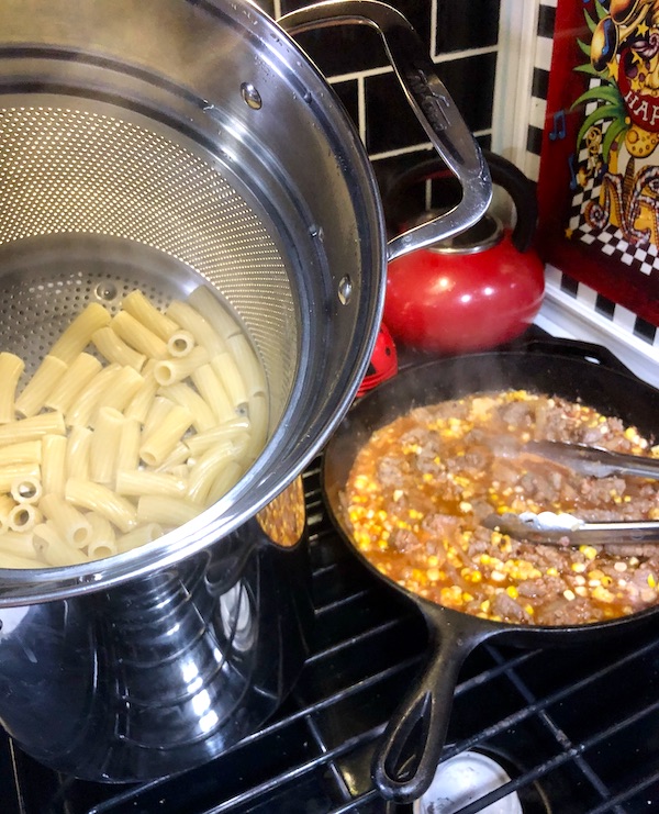 A pot of pasta draining and a pan of sauce cooking for Rigatoni with Green Cut Sausage