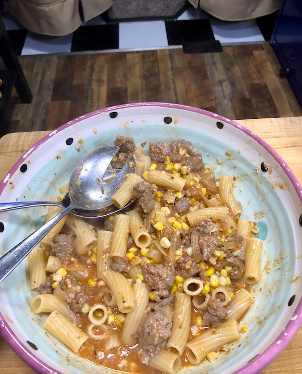 Rigatoni with Green Cut Sausage in a painted ceramic bowl with serving spoons.