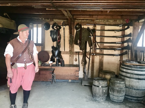 A man in colonial garb in an armory with kegs of gunpowder in Williamsburg Virginia