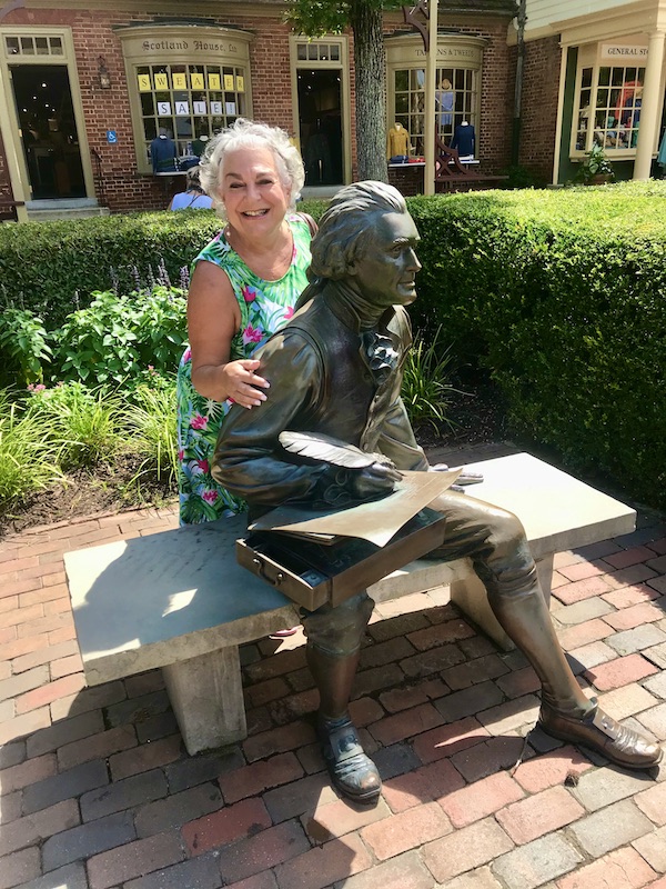 A woman behind a statue of John Hancock on a park bench in Williamsburg Virginia