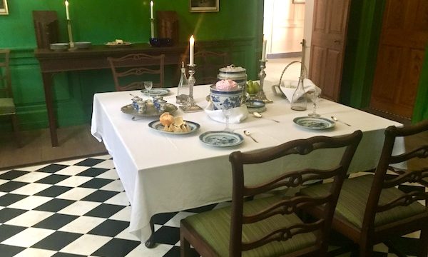 A dining room with green walls, black and white floor and square table set with white tablecloth and blue dishes at George Washington's Mount Vernon