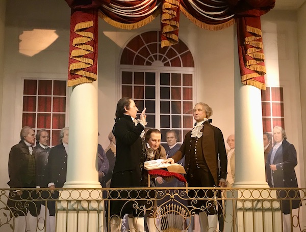 A group of men in 1700s attire on a balcony with large white pillars at George Washington's Mount Vernon
