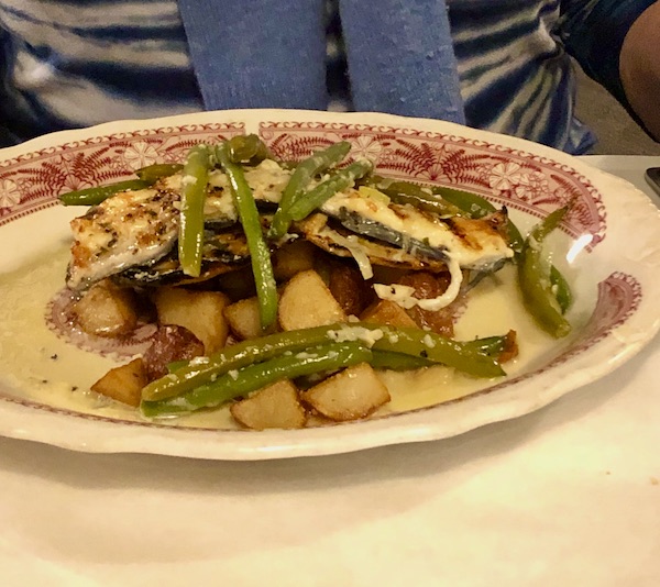 A dark red and white plate topped with potato chunks, green beans, butter sauce and a filet of fish in Atlanta Georgia