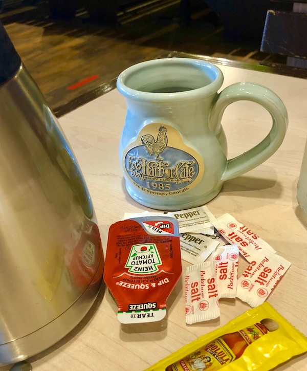 A table in a restaurant topped with a thermos, an aqua coffee mug, and packets of disposable condiments in Atlanta Georgia