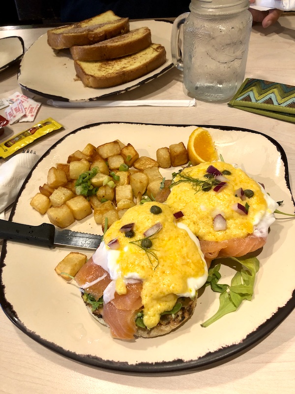 A beige plate with a brown edge topped with poached eggs, hot sauce, creamy yellow hollandaise sauce herbs and golden brown potato chunks in Atlanta Georgia