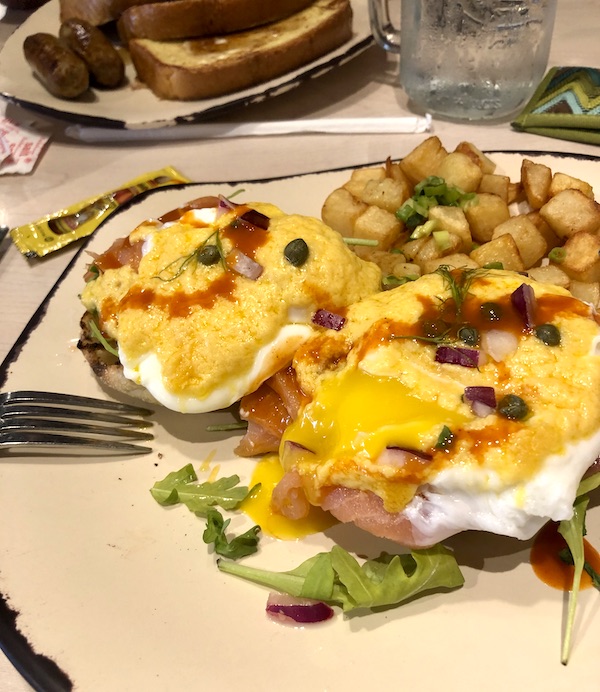 A beige plate with a brown edge topped with poached eggs, hot sauce, creamy yellow hollandaise sauce herbs and golden brown potato chunks in Atlanta Georgia