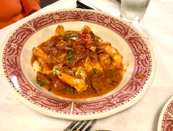 A dark red and white shallow bowl filled with shrimp, red sauce and grits in Atlanta Georgia