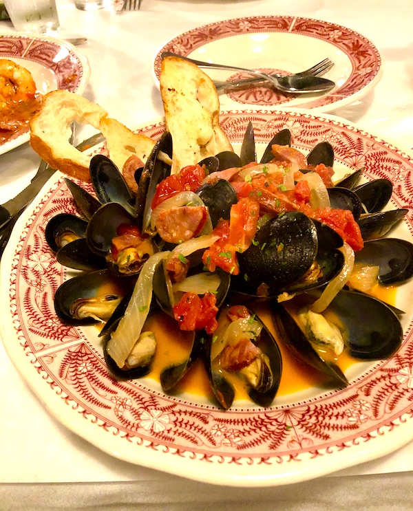 A dark red and white shallow bowl filled with mussels in their black shells, tomato broth and two slices of garlic toast in Atlanta Georgia