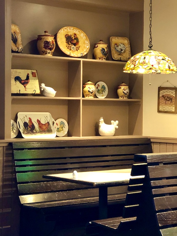 A wood slat booth in a restaurant with shelves behind displaying platters with chickens painted on them in Atlanta Georgia