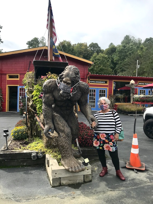 A gorilla sculpture and a woman both wearing protective masks in front of a barn near the Blue Ridge Parkway NC