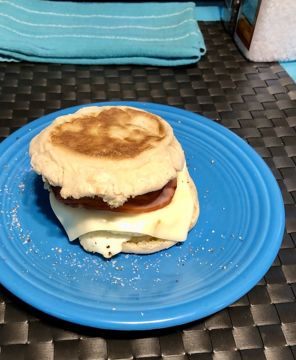 A blue plate topped with a breakfast sandwich of egg, bacon and cheese on an English muffin.