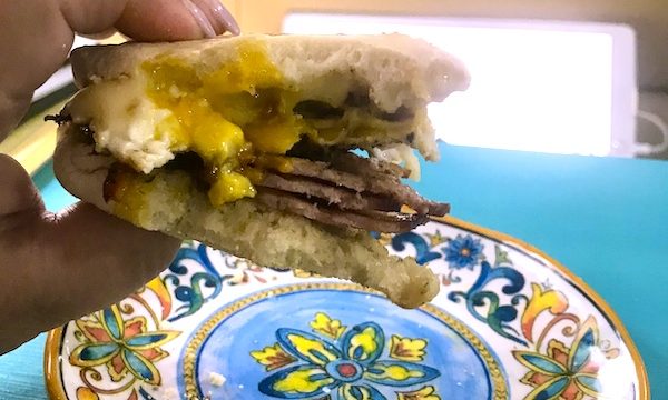 A colorful plate with a hand above it holding a breakfast sandwich with an oozy egg.