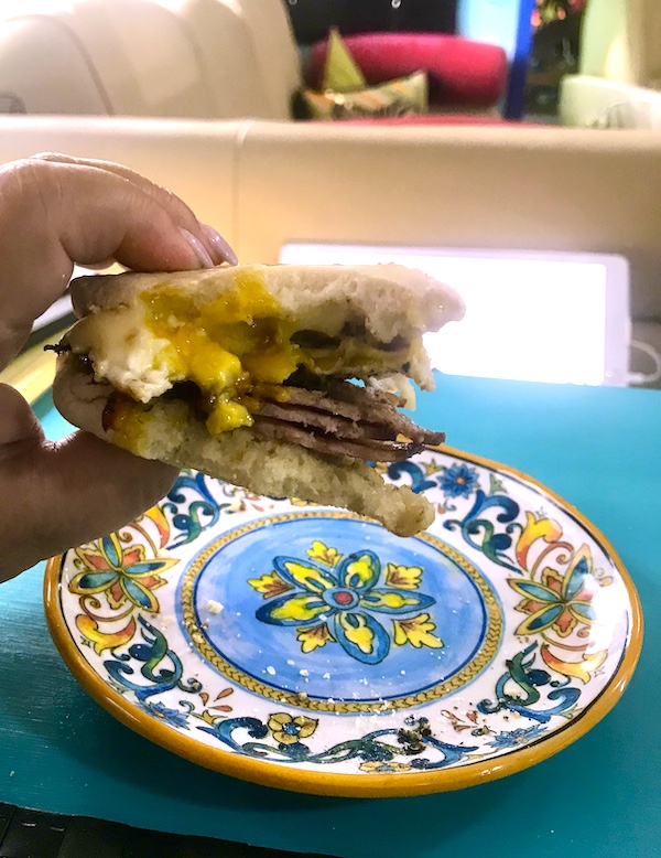 A colorful plate with a hand above it holding a breakfast sandwich with an oozy egg.