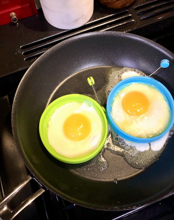 A cast iron pan with a green and a blue silicone ring holing eggs cooking for Breakfast Sandwiches