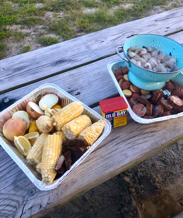 Foil pans filled with onions, corn, shrimp, sausage and potatoes on a picnic table at Delaware Seashore State Park