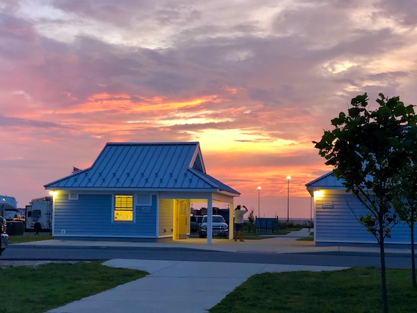A gorgeous sunset in pink, coral, yellow and lavender behind a small building at Delaware Seashore State Park