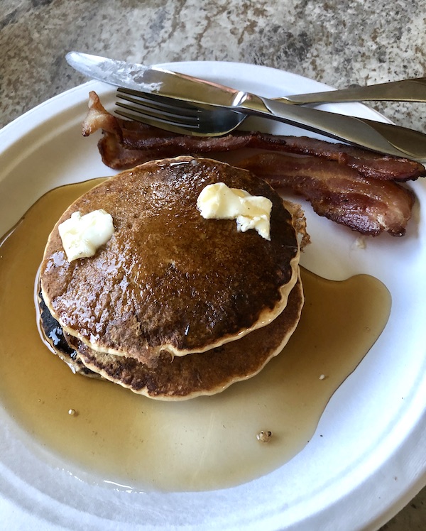 A white plate topped with a stack of pancakes, butter, syrup and bacon at Delaware Seashore State Park