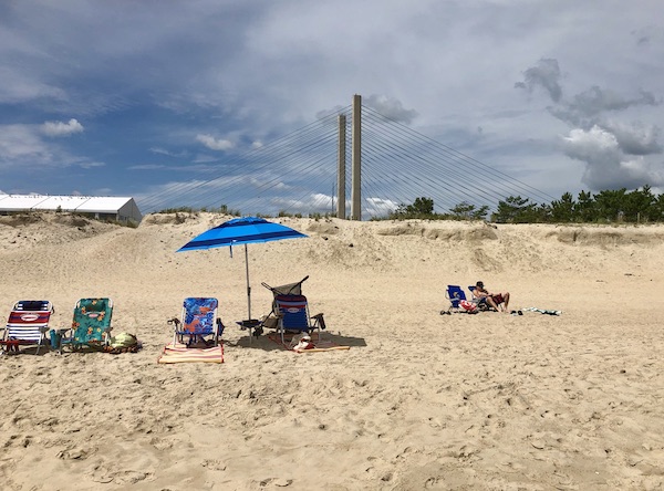 A beach with chairs, umbrellas and a bridge at Delaware Seashore State Park