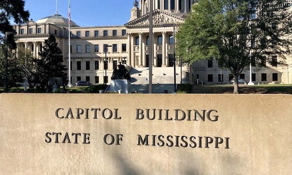 A domed white capitol building with a wall in front in Jackson Mississippi
