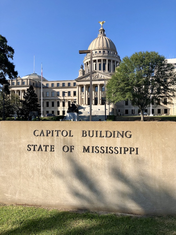 A domed white capitol building with a wall in front in Jackson Mississippi