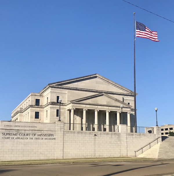 A cream colored stone building with columns and an American flag in Jackson Mississippi