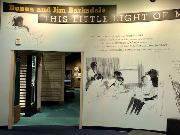 A white wall with black and white drawing depicting the creation of the song and sculpture This Little Light of Mine at the Mississippi Civil Rights Museum