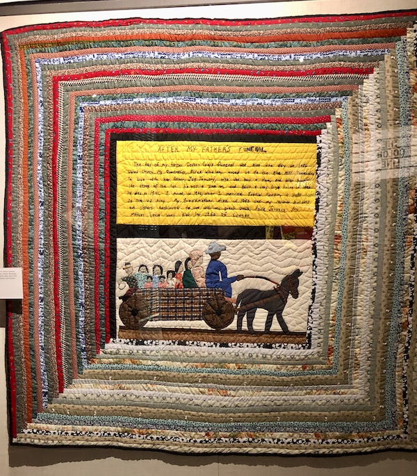A square colorful quilt showing life on a plantation at the Mississippi Civil Rights Museum