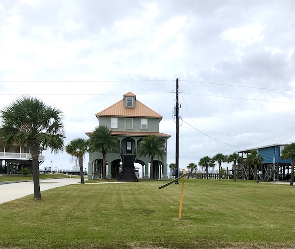 A stilt home with a barren tile roof set on a large lawn and lots of palm trees along our route from NOLA to Biloxi