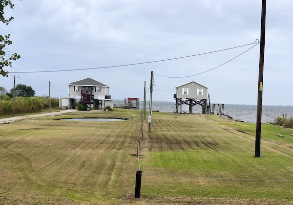 Two houses built up on stilts with large lawn in front and water in back on our drive from NOLA to Biloxi