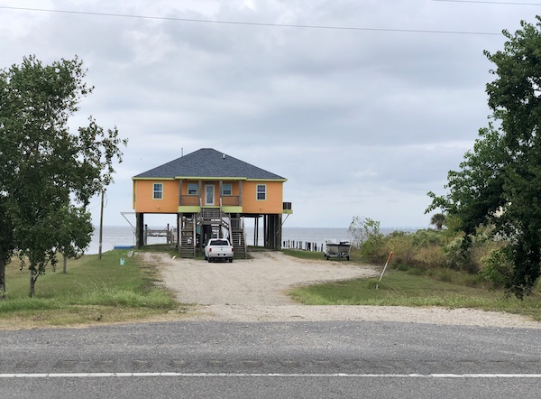 A bright yellow stilt home with water behind it on our drive from NOLA to Biloxi