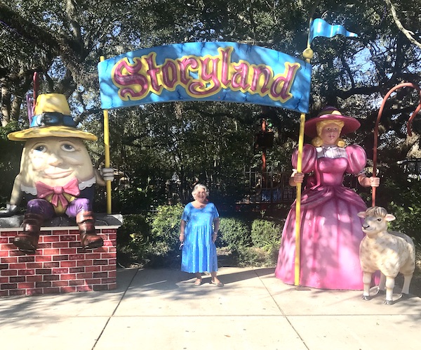 An arched entrance to Storyland with huge storybook characters and a silver haired woman in a blue dress at New Orleans City Park