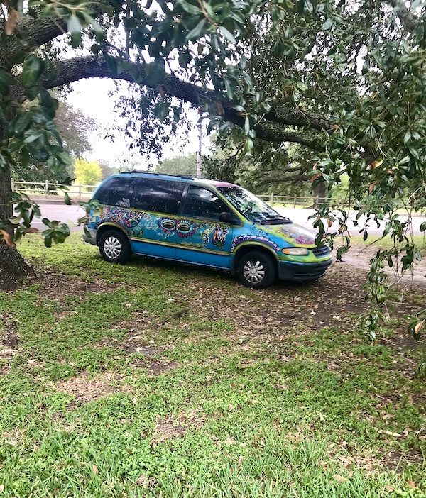 A blue van parked under trees and painted colorfully at New Orleans City Park