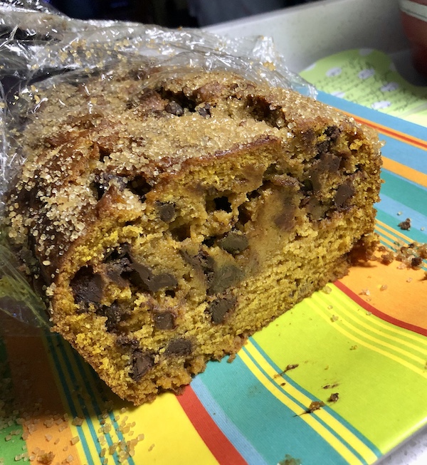 A partially cut loaf cake on a striped plate is a Pumpkin Chocolate Chip Loaf