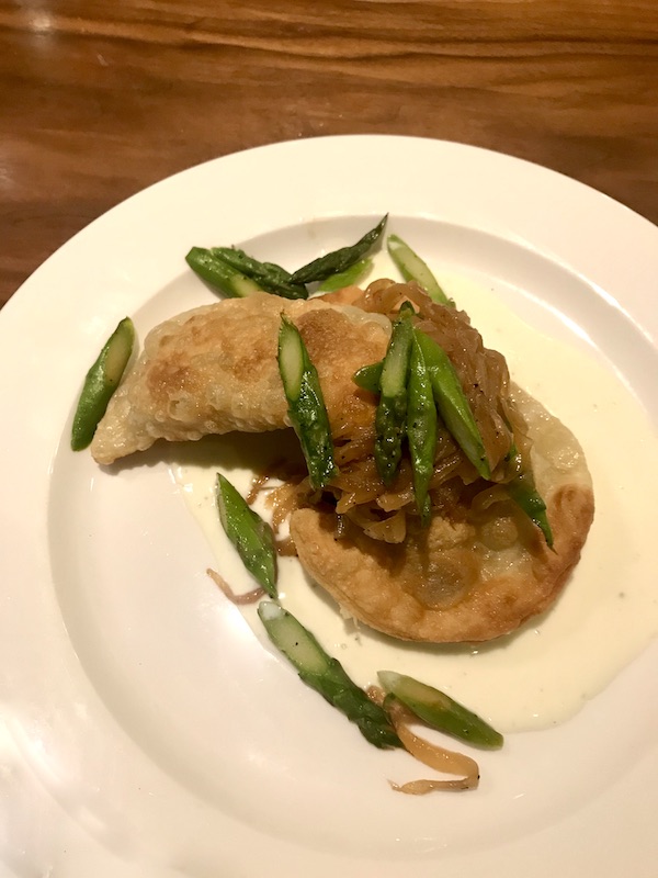 A white plate topped with fried pasta crescents with caramelized onions and slices of asparagus at Sue Zemanick's Zasu