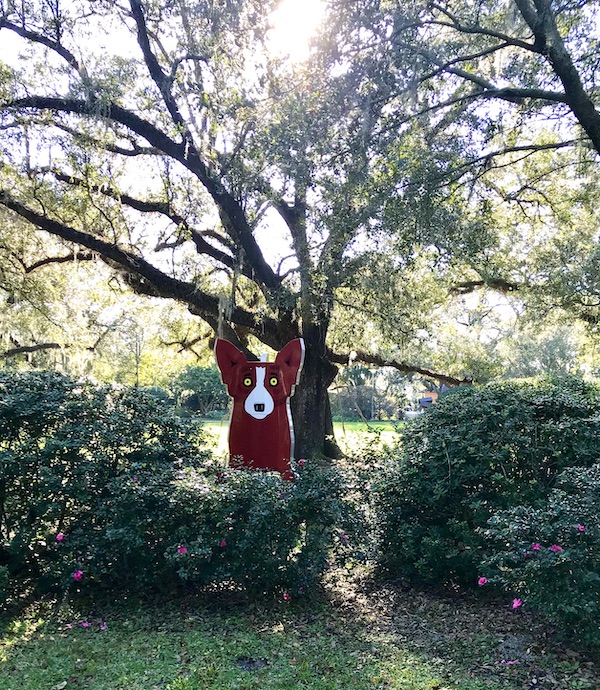 A sculpture of a red dog by a tree at the Bestoff Sculpture Garden